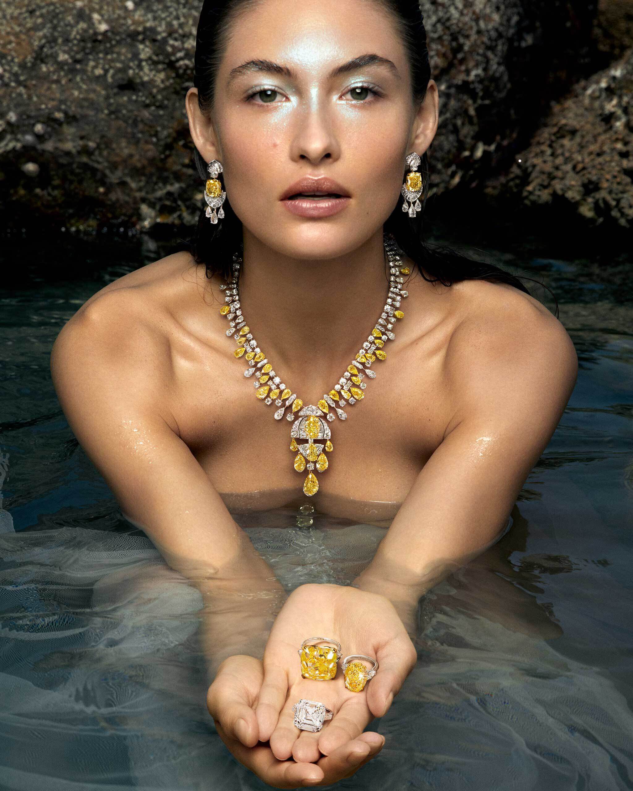 Model wearing Graff yellow and white diamond necklace and earrings and holding three Graff yellow and white diamond rings in her hands