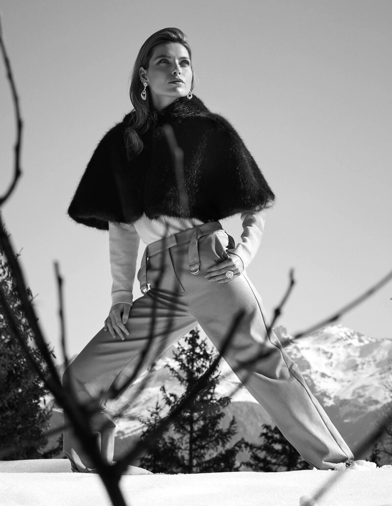 A lady on a ski slope dressed in a fur cape and wearing diamond Luna earrings and a diamond Swirl ring
