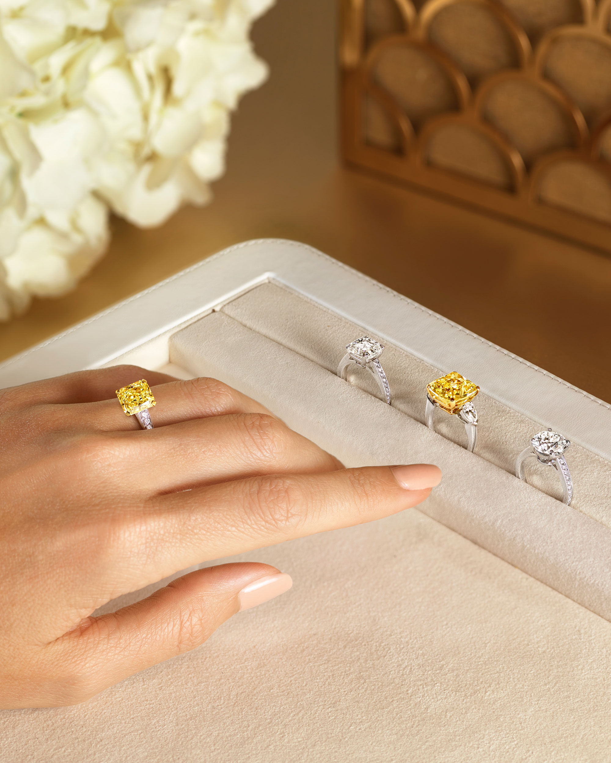 Close up of a model wearing a Graff yellow diamond ring with three diamond rings on a tray
