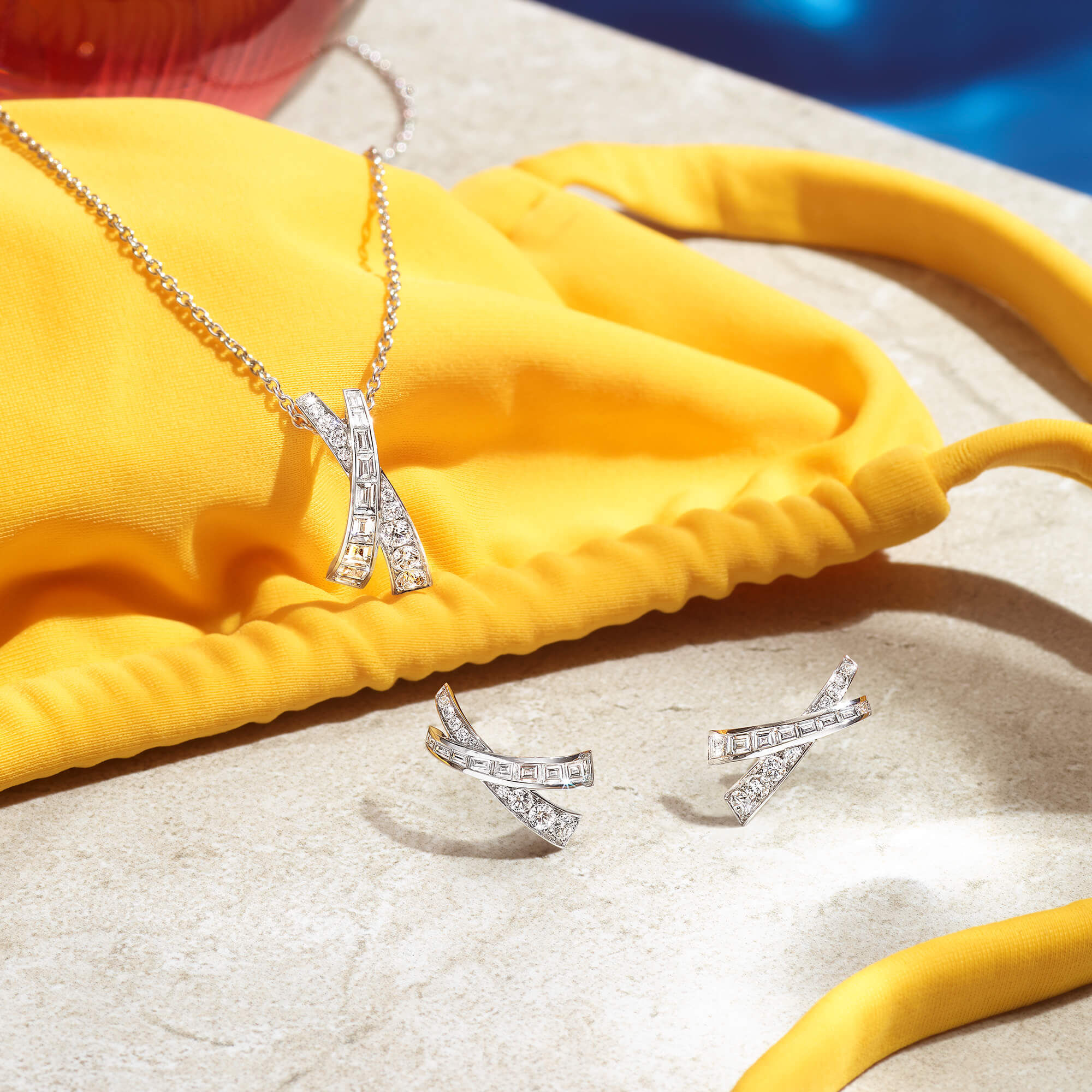 Close up of the Graff Kiss collection diamond earrings and pendant at a pool side