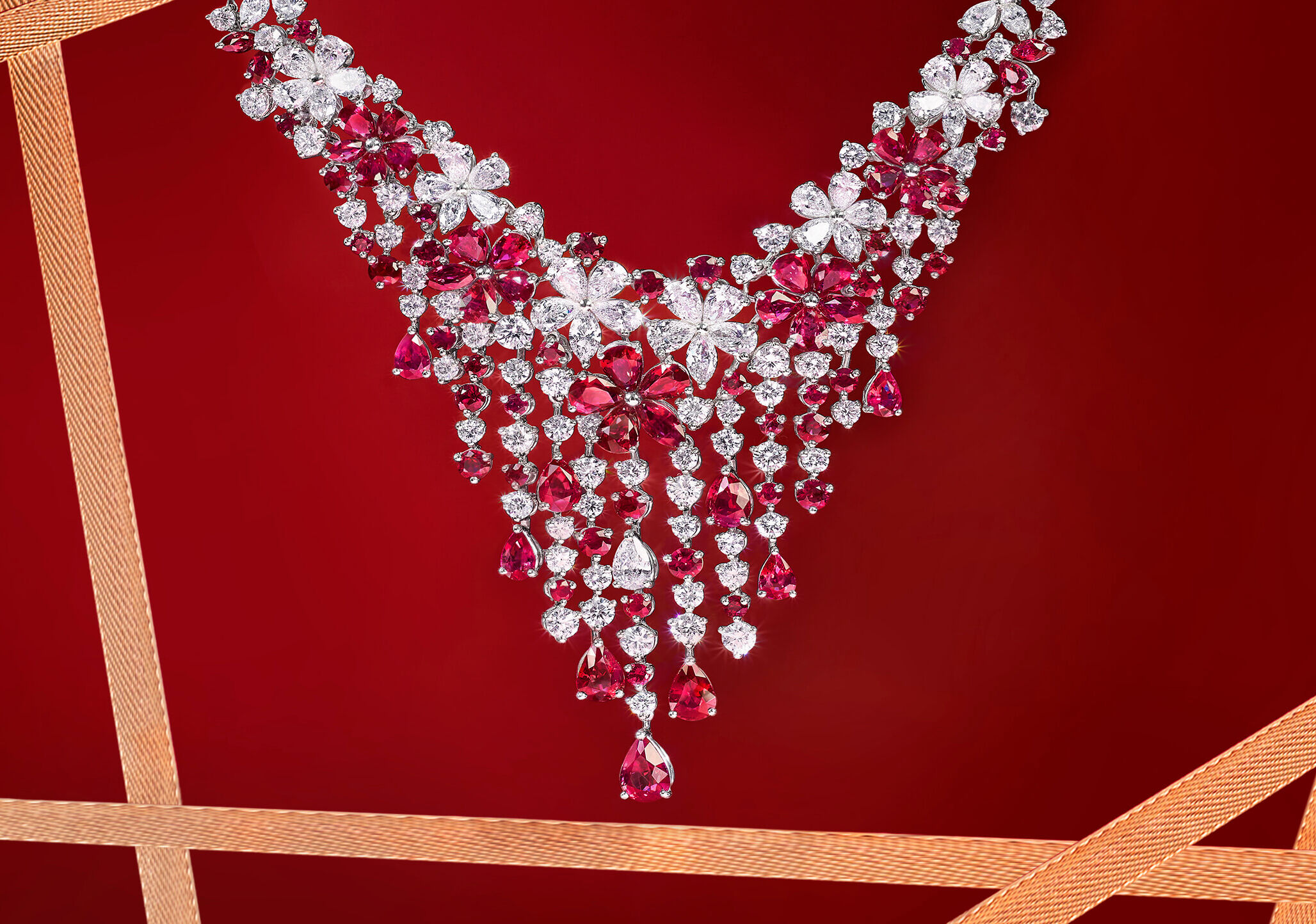 A Graff Carissa Collection Ruby and Diamond Necklace hanging in front of a red background with gold ribbons
