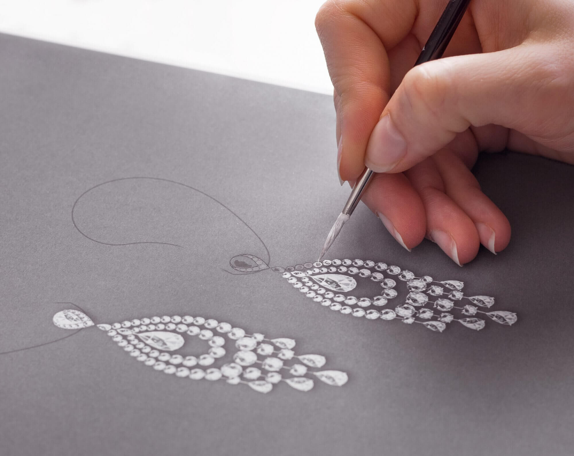 A designer hand paints a detailed two-dimensional representation of how a the earrings might look