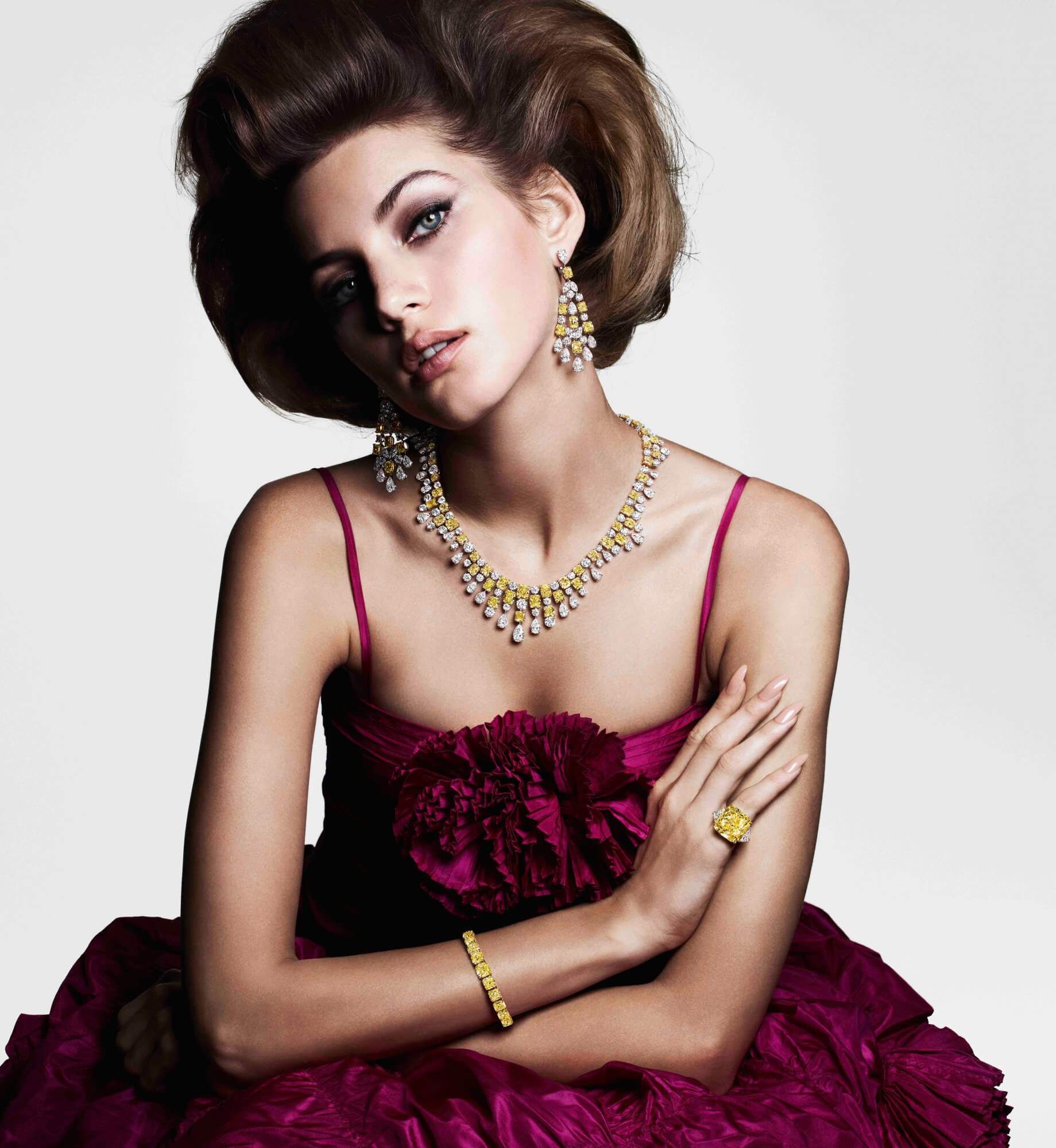 A model wearing Graff yellow and white diamond high jewellery earrings necklace ring and bracelet in a purplish red evening gown
