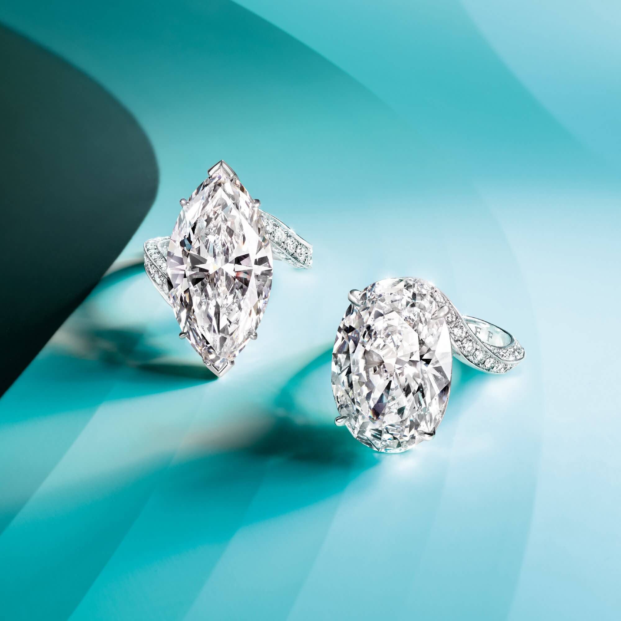 Two Graff diamond rings featuring a marquise shape diamond and an oval shape diamond respectively on light blue background