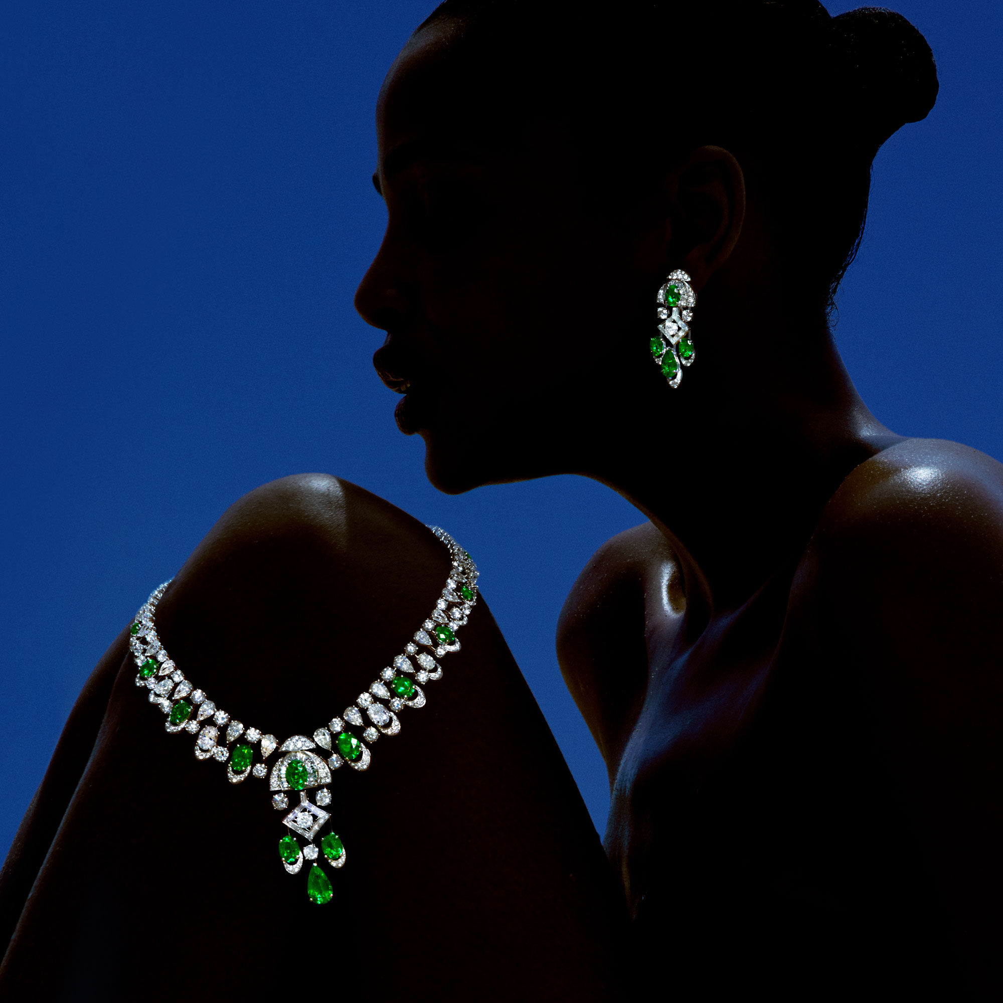 Navy blue silhouette of a model with emerald and diamond high jewellery earrings and necklace