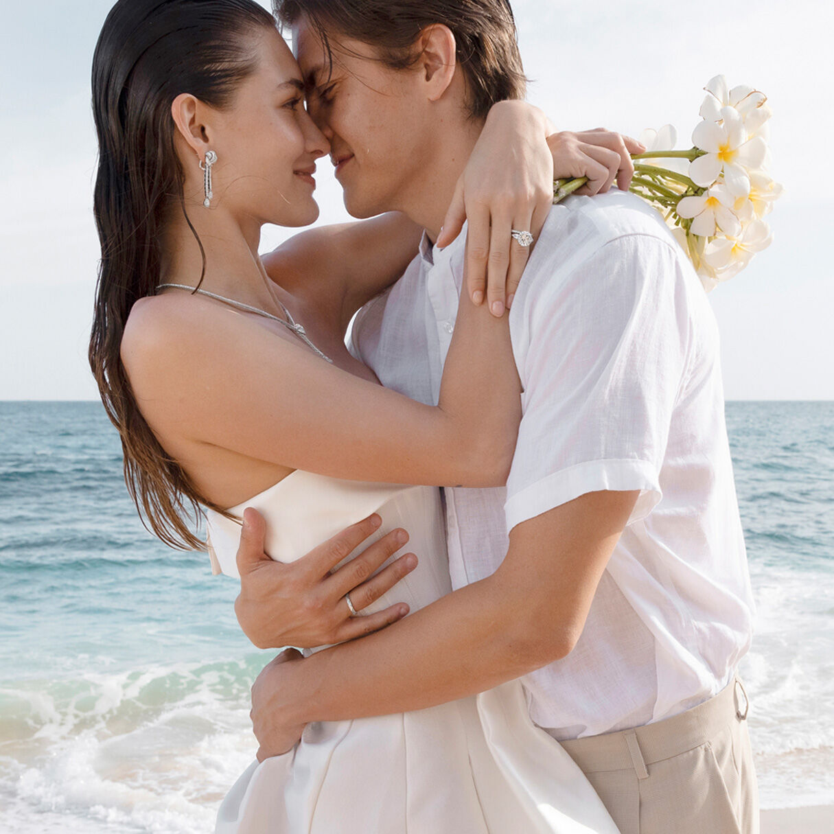 Female and male model on beach, female model wearing Graff Diamond engagement ring and wedding band and Graff Bridal Jewellery Suite