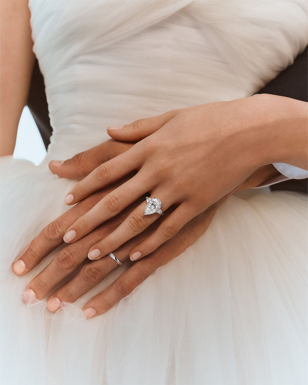 Image shows female and male model hands wearing Graff Promise Pear Shape engagement ring and spiral wedding band