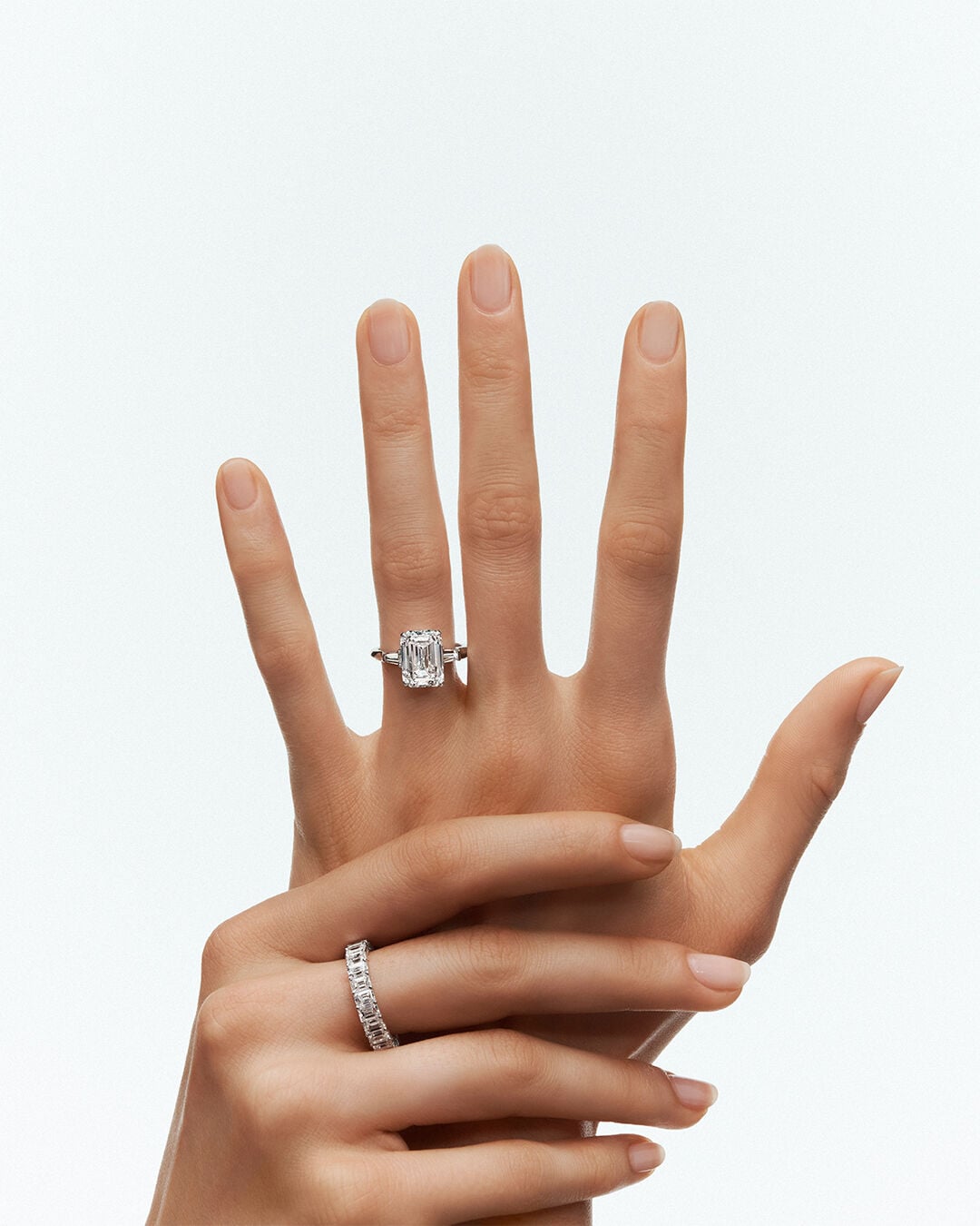 Image shows model hand wearing Graff Emerald Cut Promise diamond engagement ring and Emerald Cut diamond eternity ring