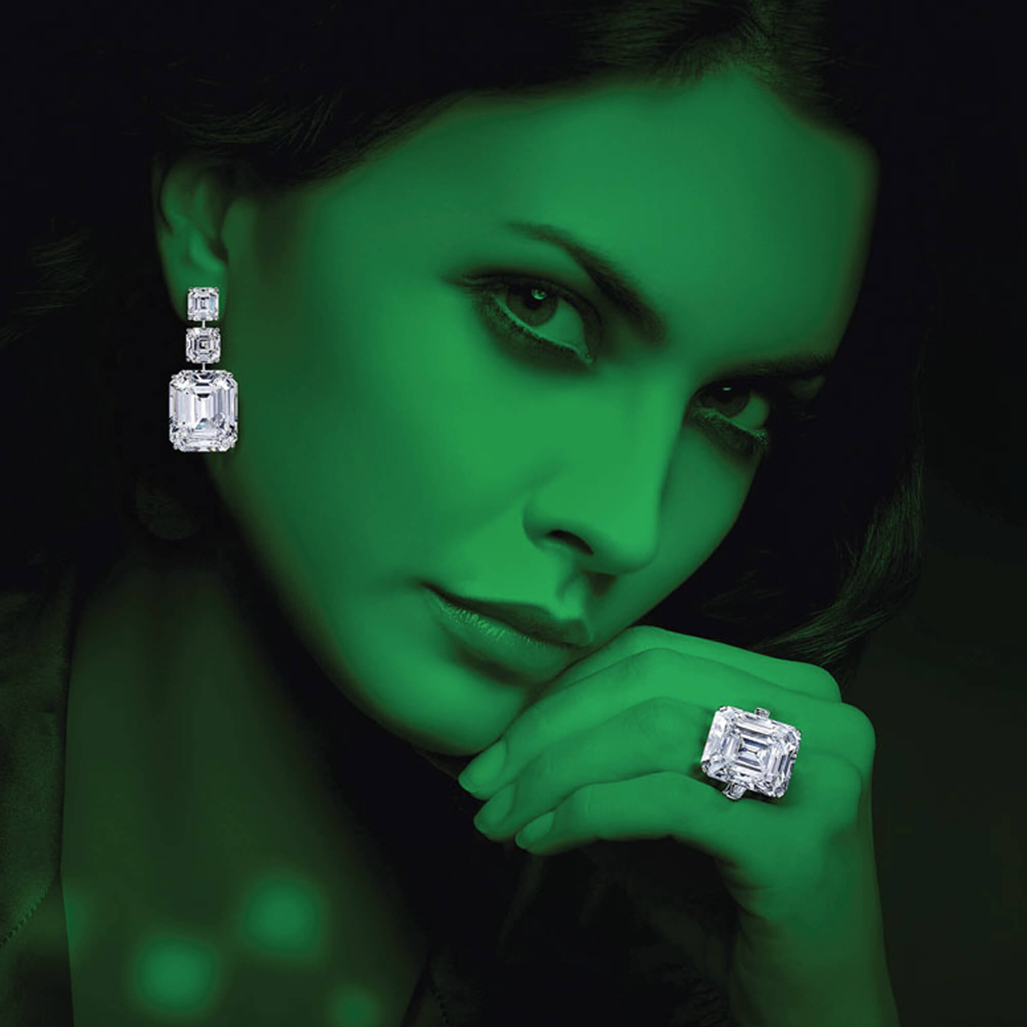 Model with green effect wearing Graff high jewellery emerald cut earrings and emerald cut solitaire ring.