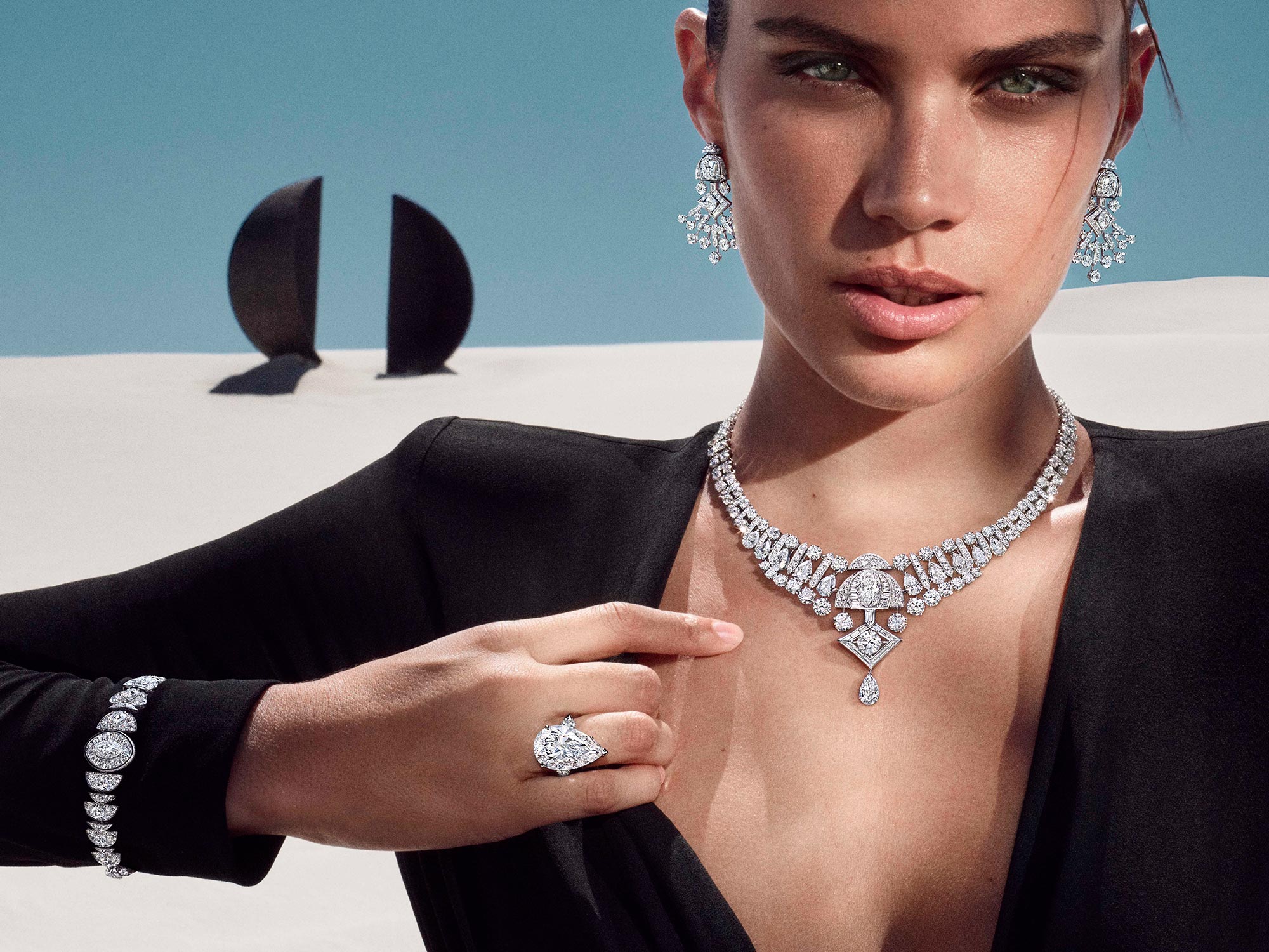 Close up of a model wearing Graff Nigh Moon white diamond earrings, bracelet and necklace from the Tribal jewellery collection and a pear shape diamond ring, in a desert